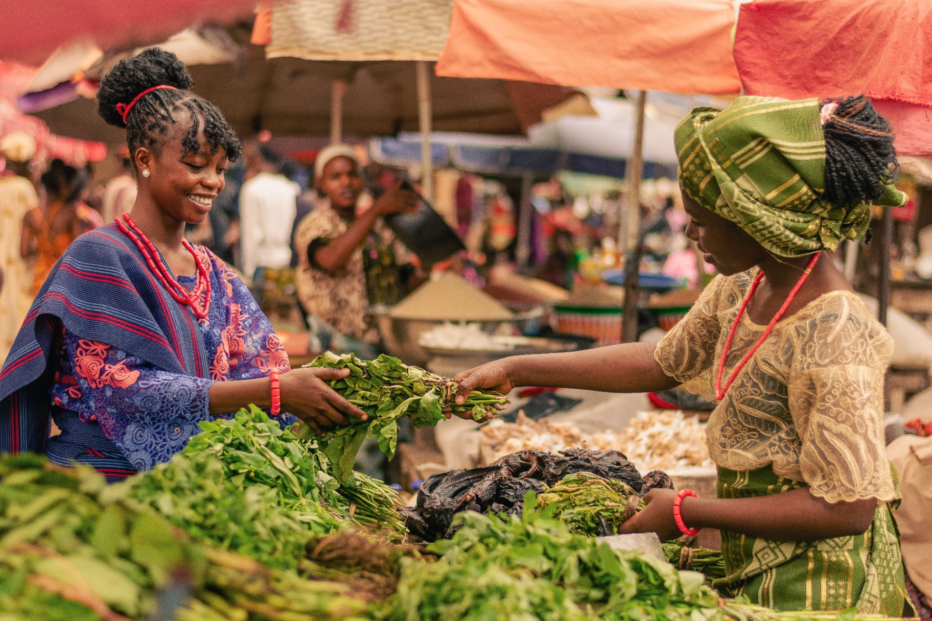 Two women trading fresh greens at a busy market stall